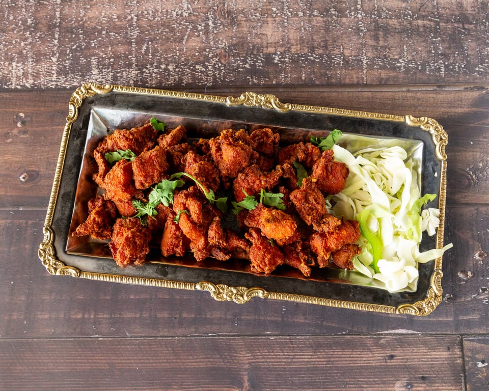 A silver and gold ornate tray filled with crispy fried chicken pieces and shredded cabbage.