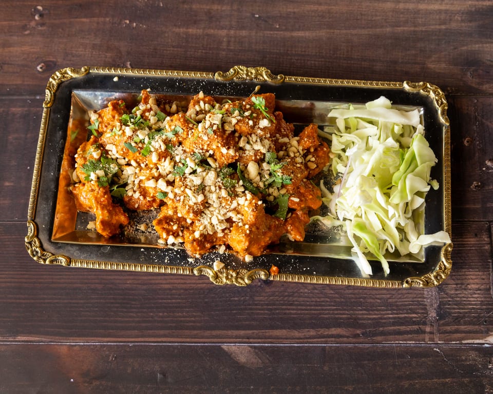 Orange chicken with peanuts and cilantro, alongside shredded cabbage, on a silver tray.