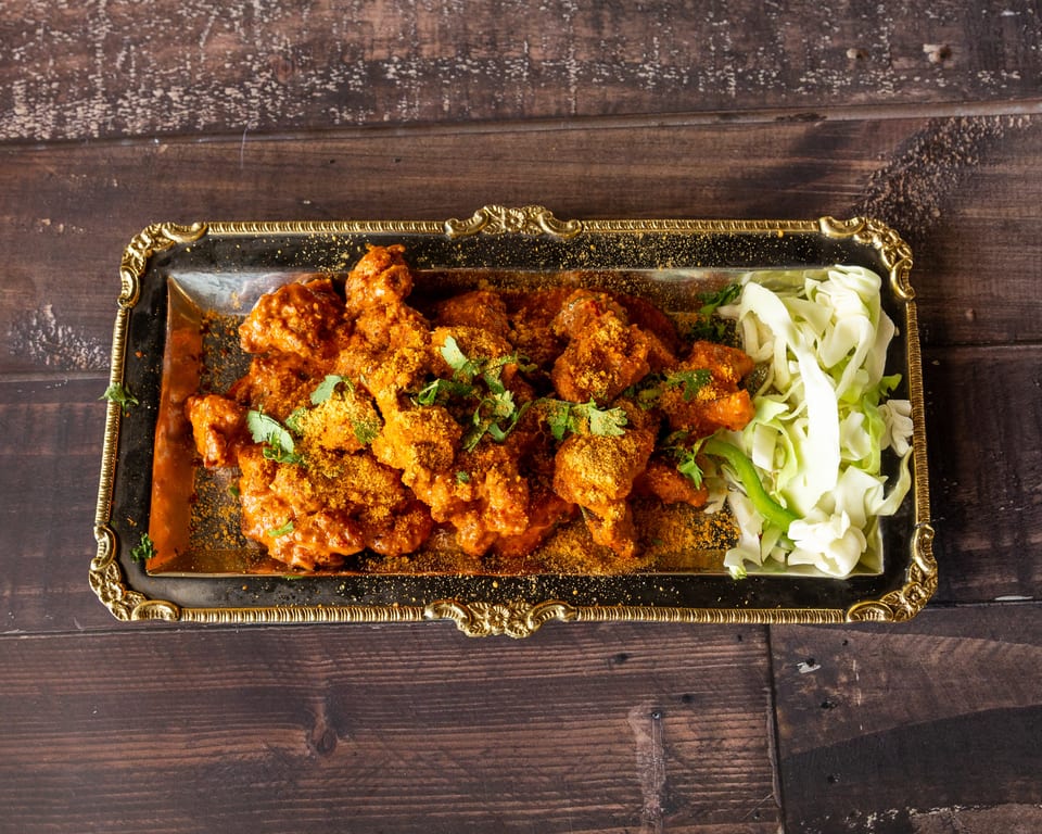 Chicken 65, a South Indian fried chicken dish, served on a silver platter with shredded cabbage.