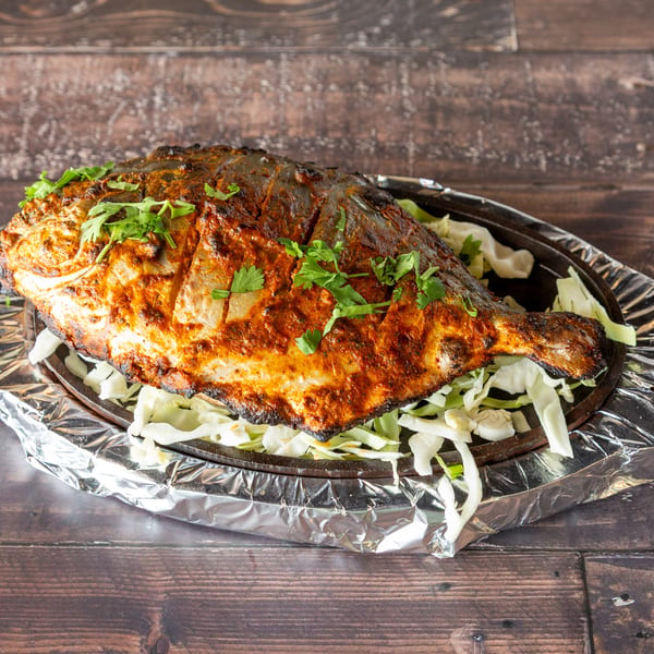 Whole grilled fish, seasoned with spices and herbs, served on a bed of shredded cabbage.