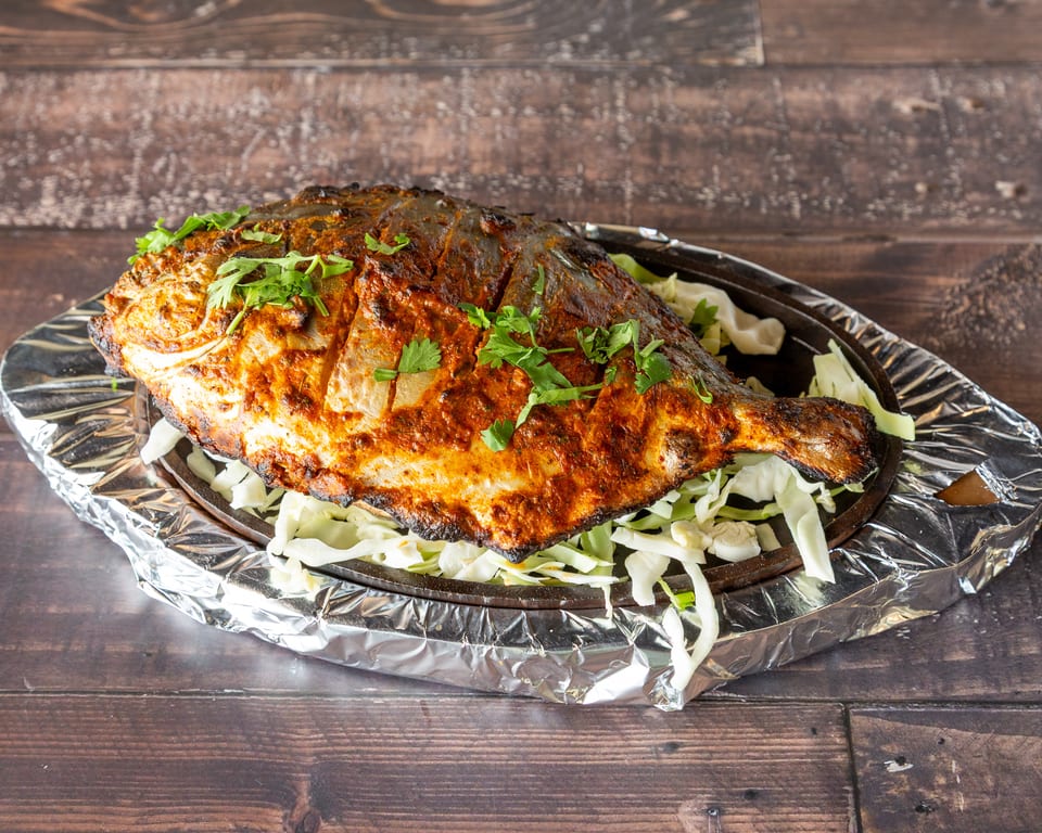 Whole grilled fish, seasoned with spices and herbs, served on a bed of shredded cabbage.
