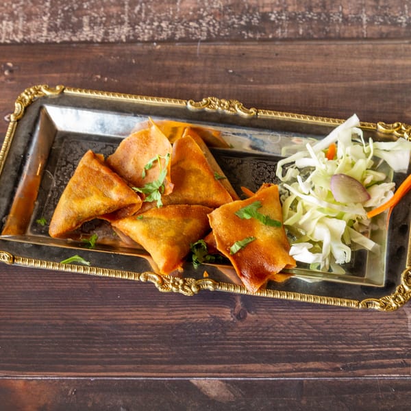 Golden-brown samosas garnished with cilantro and a side of shredded cabbage and carrots on a silver tray.
