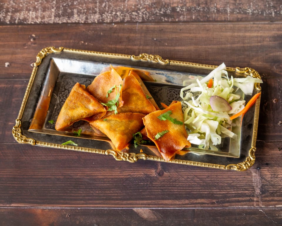 Golden-brown samosas garnished with cilantro and a side of shredded cabbage and carrots on a silver tray.