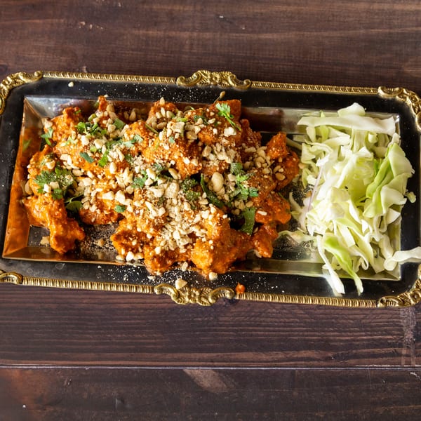 Orange chicken with peanuts and cilantro, served with shredded cabbage on a silver tray.