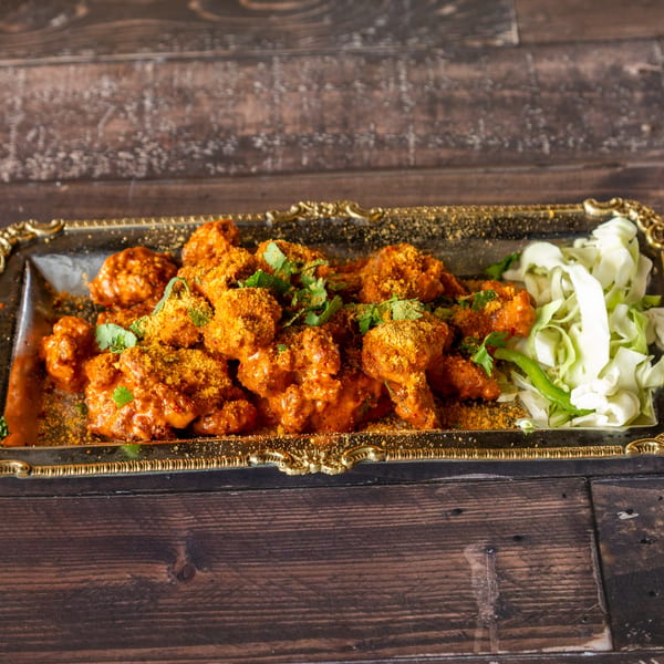 Spicy orange chicken wings with cilantro and shredded cabbage on a gold-rimmed tray.