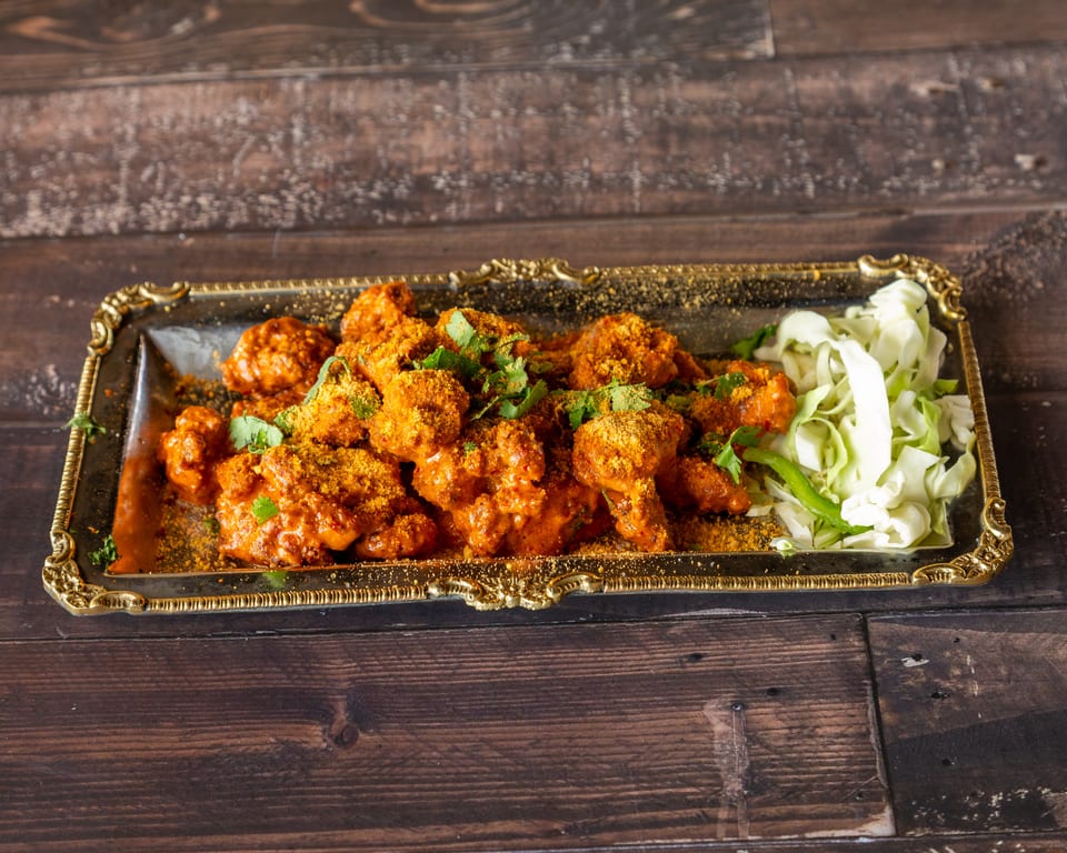 Spicy orange chicken wings with cilantro and shredded cabbage on a gold-rimmed tray.