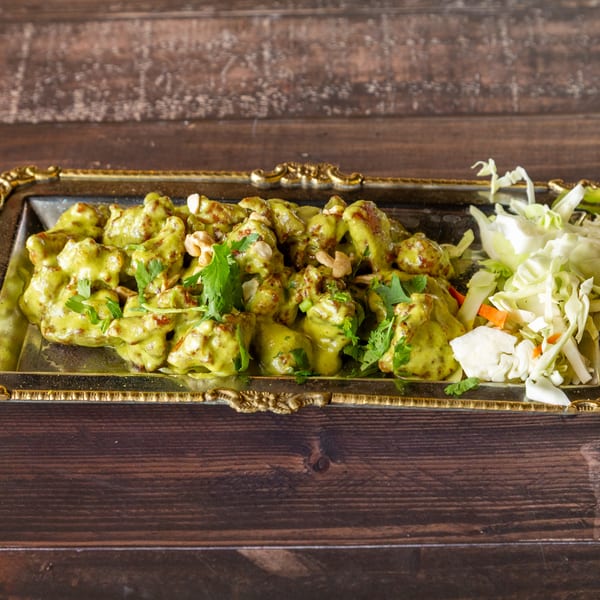Green curry chicken with cashews and cilantro, served with shredded cabbage on a gold-rimmed tray.
