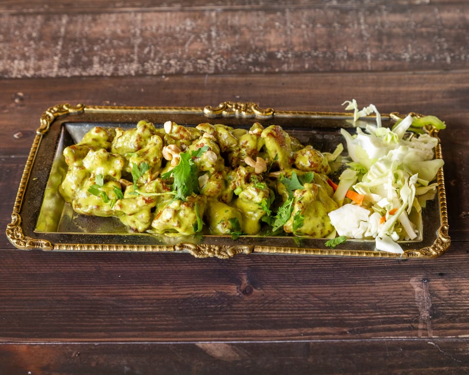 Green curry chicken with cashews and cilantro, served with shredded cabbage on a gold-rimmed tray.