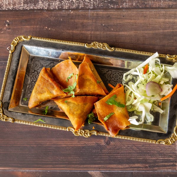 Golden-brown samosas with fresh cilantro and a side of shredded cabbage salad on a silver tray.