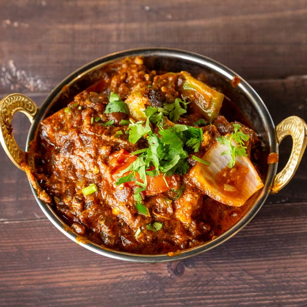 A close-up of a vibrant Indian curry with vegetables and cilantro in a brass bowl.