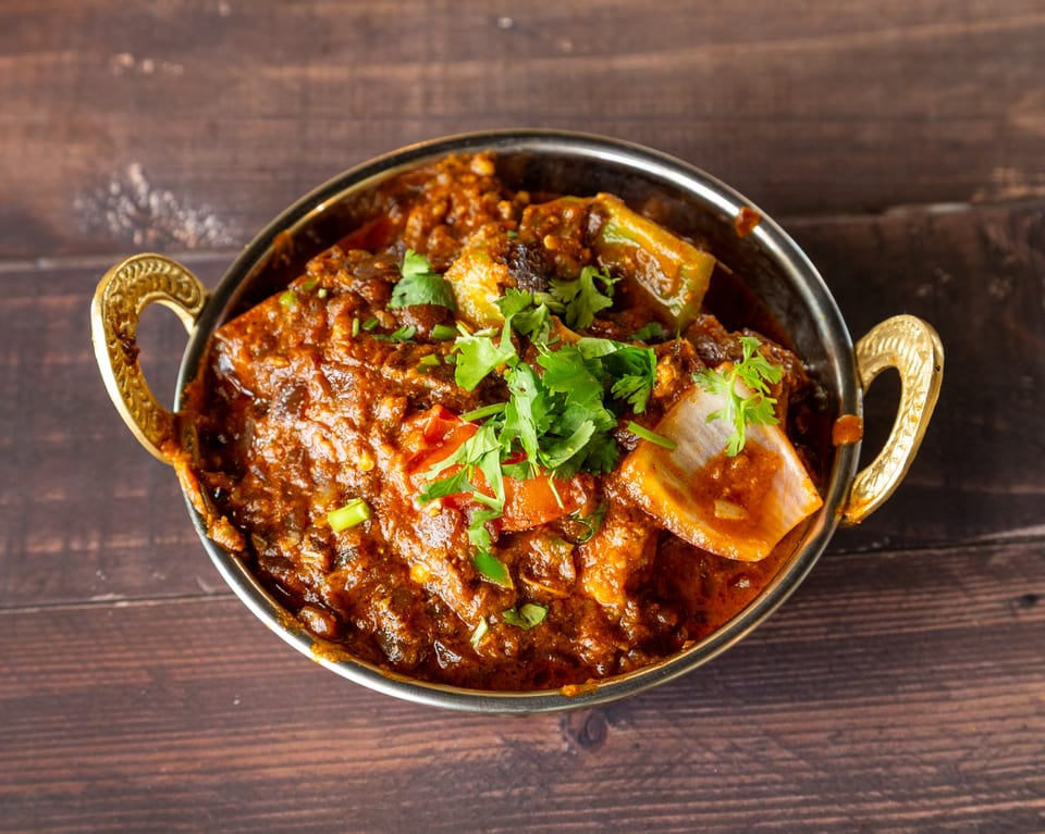 A close-up of a vibrant Indian curry with vegetables and cilantro in a brass bowl.