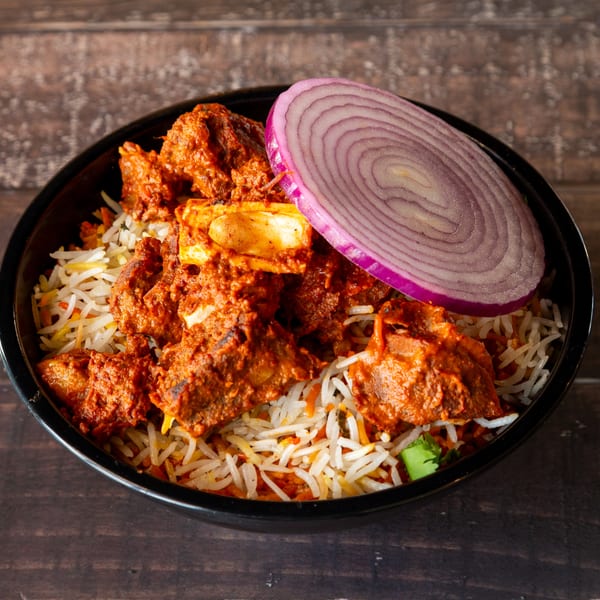 Spicy lamb biryani with basmati rice and a slice of red onion in a black bowl.