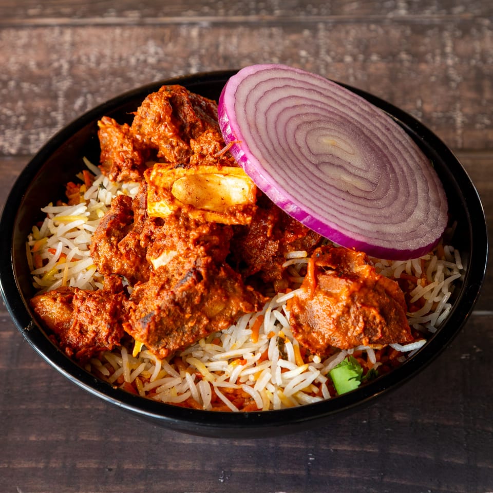Spicy lamb biryani with basmati rice and a slice of red onion in a black bowl.