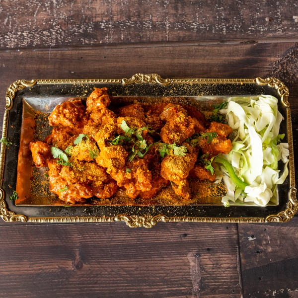 Chicken 65, a South Indian fried chicken dish, served on a gold-rimmed platter with shredded cabbage.