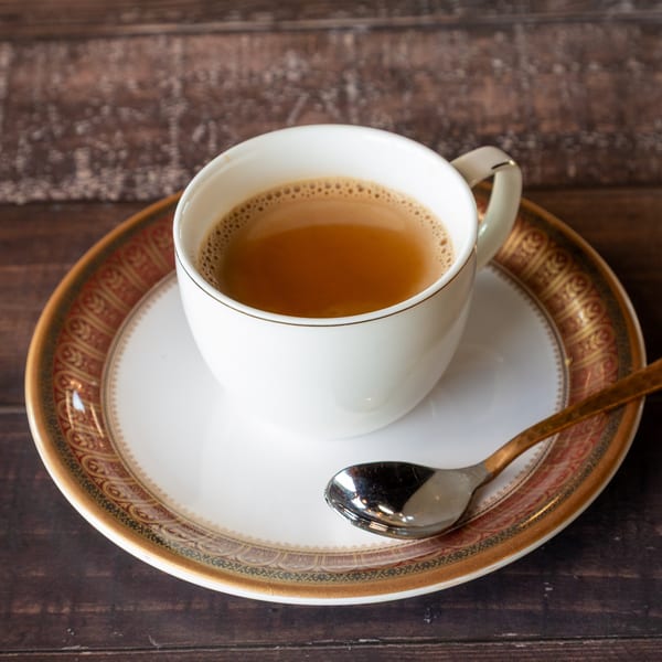 A white cup of chai tea with a spoon on a decorative saucer, on a dark wooden table.