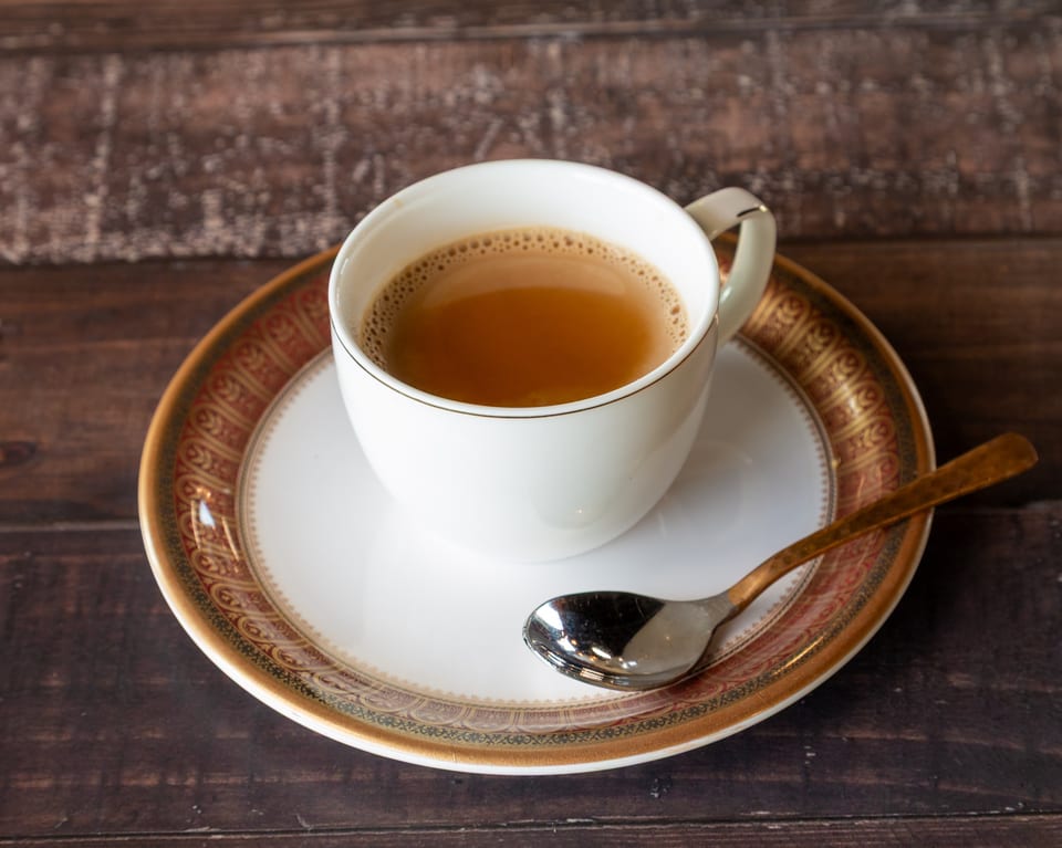 A white cup of chai tea with a spoon on a decorative saucer, on a dark wooden table.