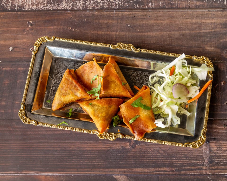 Golden-brown samosas with fresh cilantro and a side of shredded cabbage salad on a silver tray.
