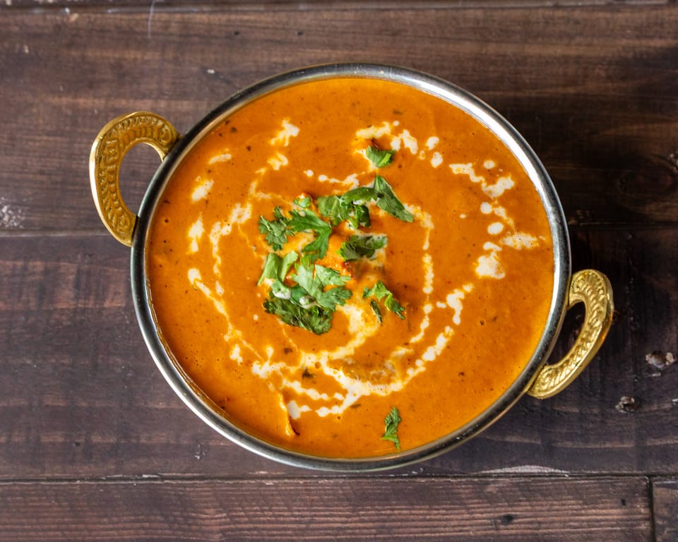 Overhead view of a golden bowl of orange curry with cream swirls and fresh cilantro.