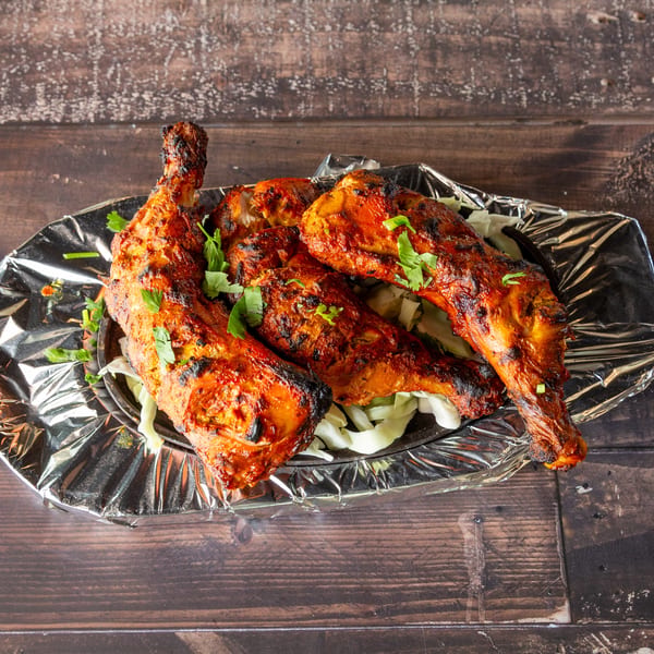 Four grilled chicken legs with herbs on a bed of shredded cabbage, served on a foil-lined tray.