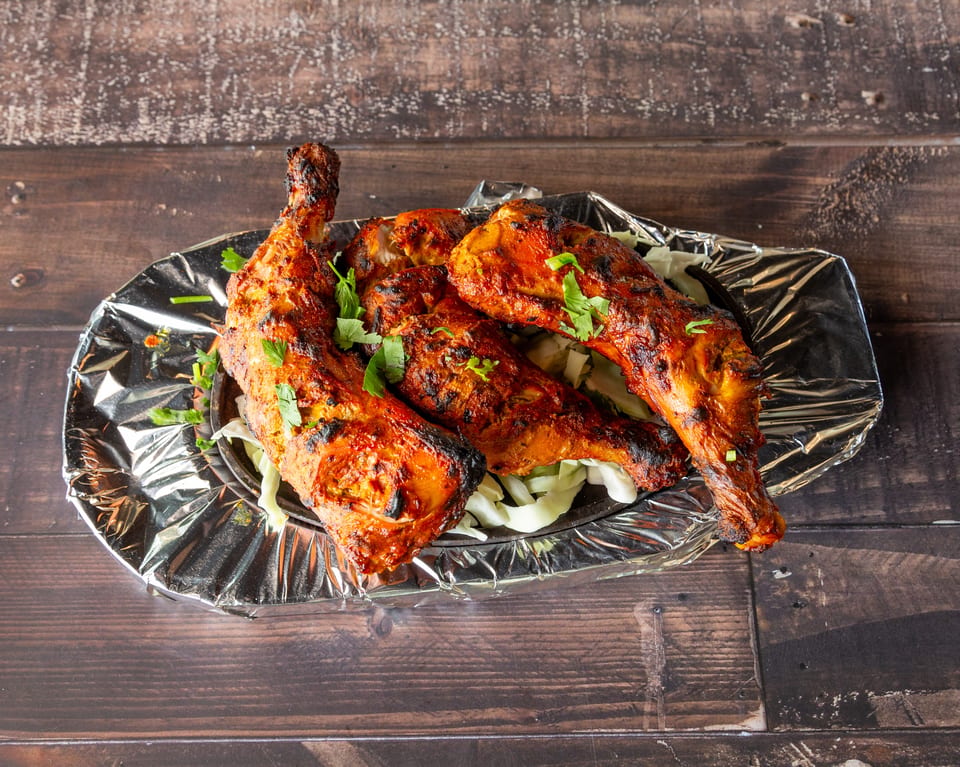 Four grilled chicken legs with herbs on a bed of shredded cabbage, served on a foil-lined tray.