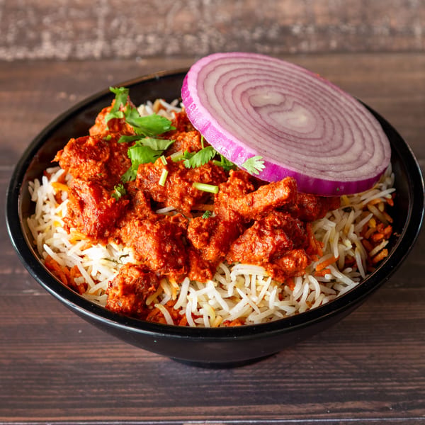 Chicken tikka biryani with white rice, red chicken pieces, cilantro, and a red onion slice.