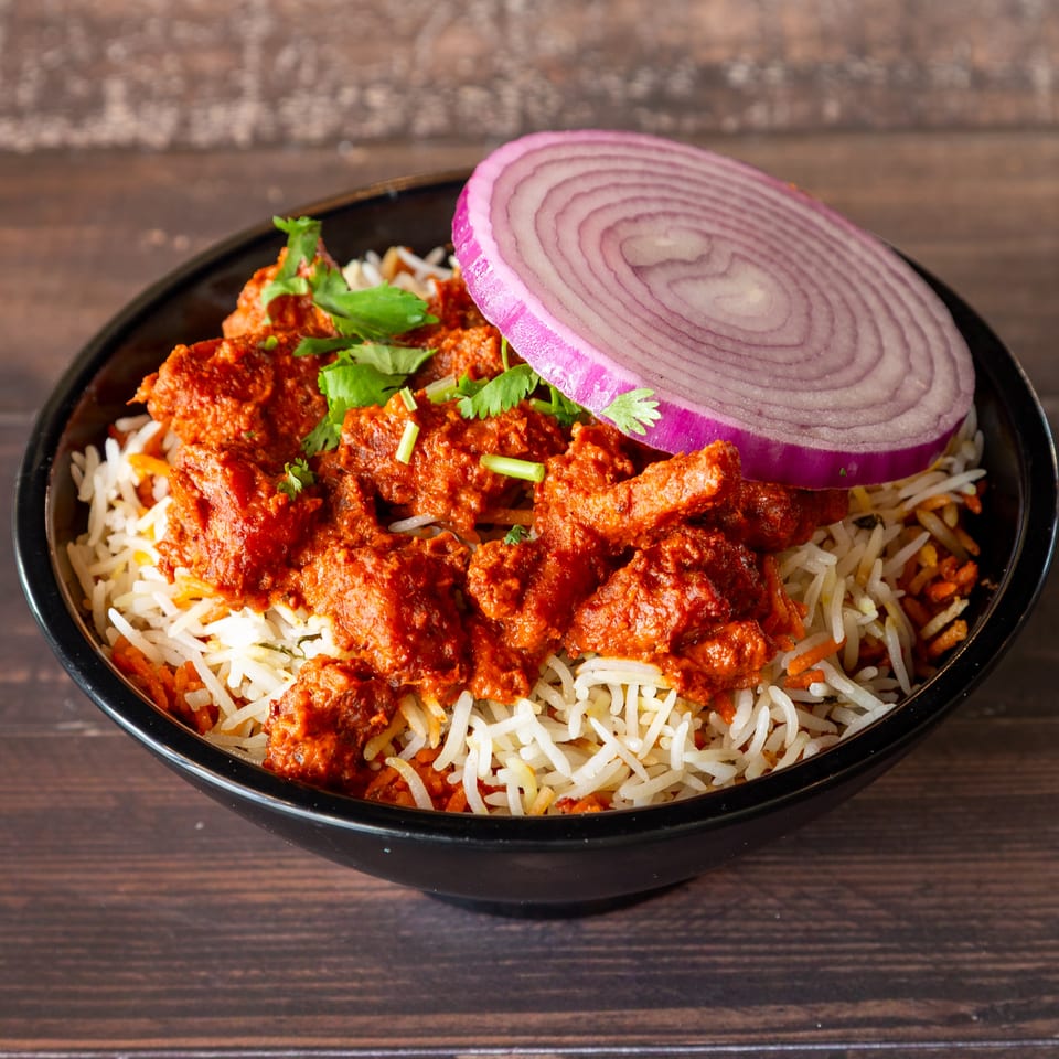 Chicken tikka biryani with white rice, red chicken pieces, cilantro, and a red onion slice.
