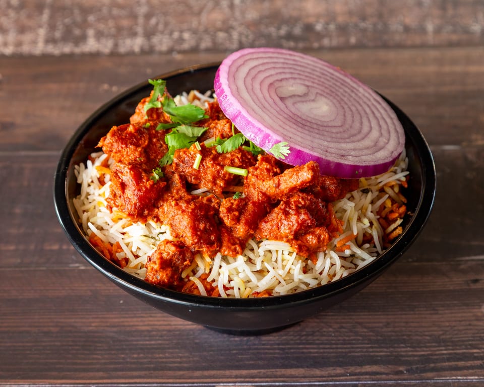 Chicken tikka biryani with white rice, red chicken pieces, cilantro, and a red onion slice.