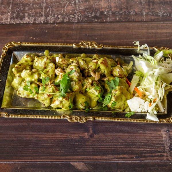 Chicken in green sauce with cashews and cilantro, served with shredded cabbage on a gold tray.