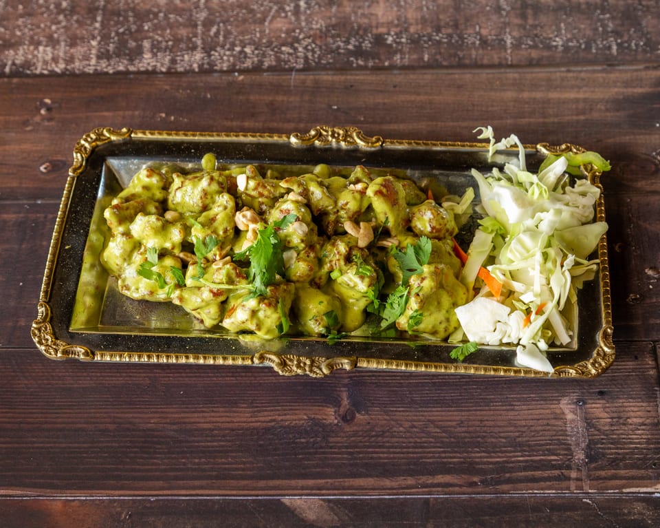 Chicken in green sauce with cashews and cilantro, served with shredded cabbage on a gold tray.