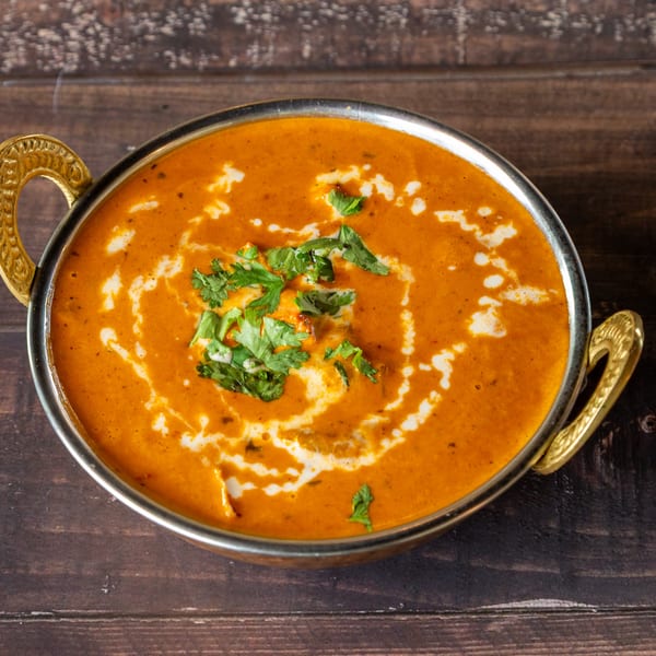 A golden bowl of creamy orange curry, garnished with fresh cilantro and a swirl of cream.