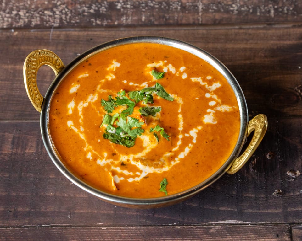 A golden bowl of creamy orange curry, garnished with fresh cilantro and a swirl of cream.