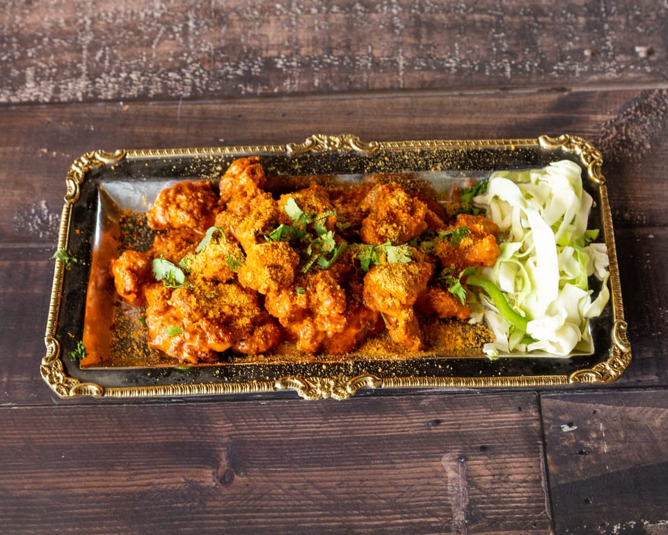 Spicy chicken wings with seasoning and fresh cabbage on a gold-rimmed platter.