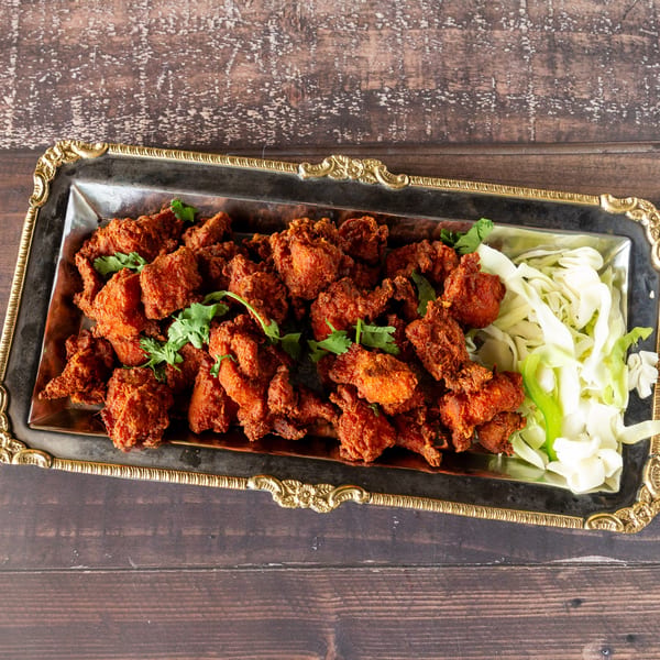 A silver platter of crispy fried chicken pieces with cilantro and shredded cabbage on a wooden table.