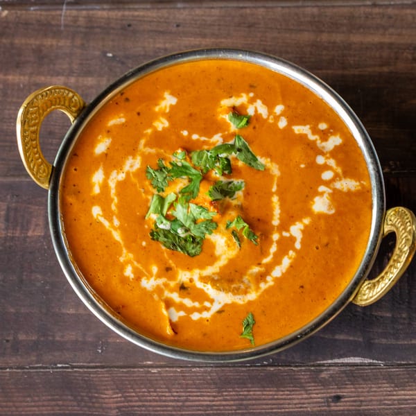 Overhead view of a golden bowl filled with orange curry, garnished with cream swirls and fresh cilantro.